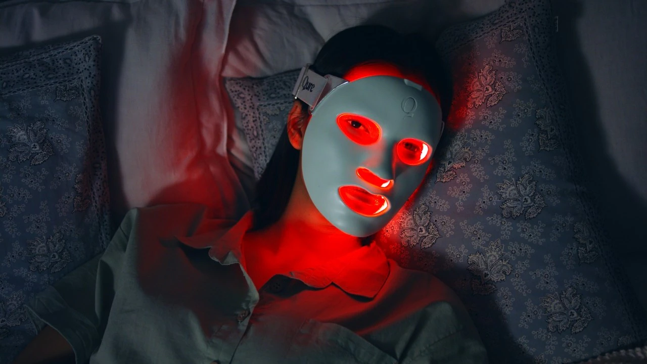 Woman using an LED light therapy face mask at home LED skincare mask glowing red while applied on face